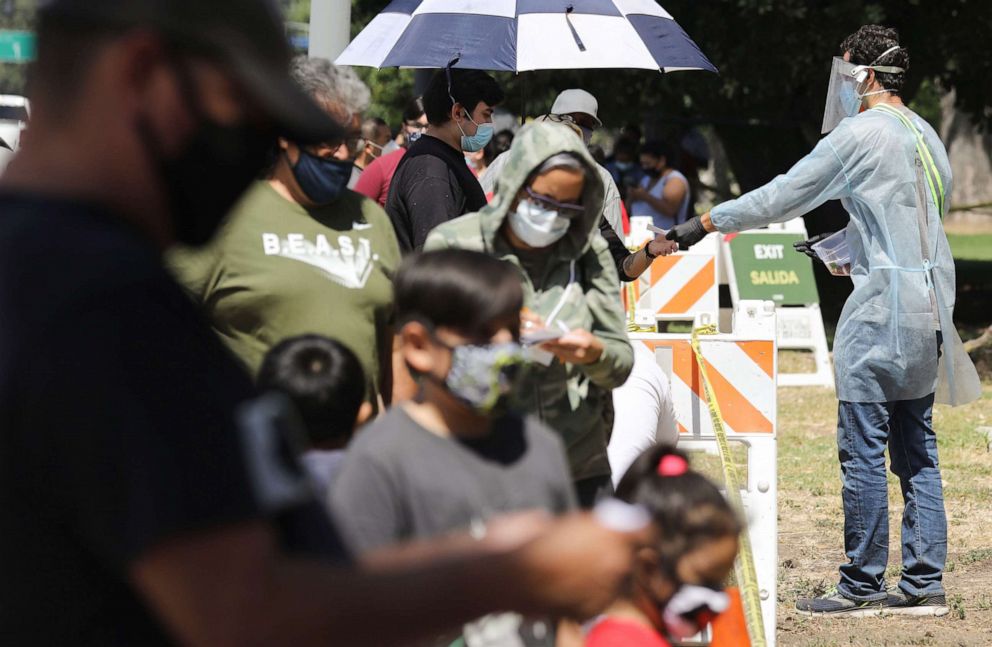 PHOTO: A testing associate dressed in personal protective equipment helps people waiting in line to check in at a COVID-19 testing center at Lincoln Park amid the coronavirus pandemic on July 07, 2020, in Los Angeles.
