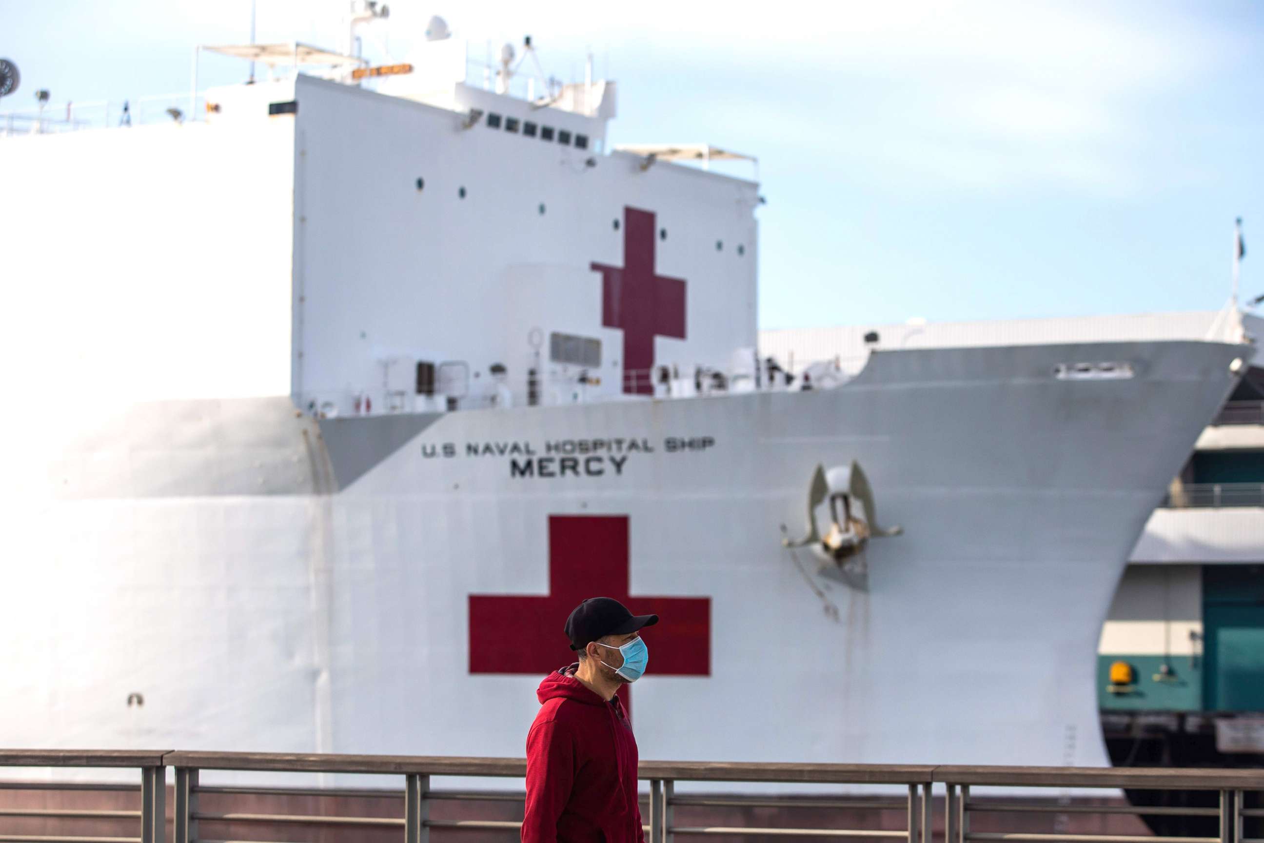 PHOTO: A man walks wearing facemak as a preventive measure against the spread of the coronavirus in front of the US Navy Hospital ship Mercy, March 28, 2020, at the Port of Los Angeles in the city of San Pedro, Calif.