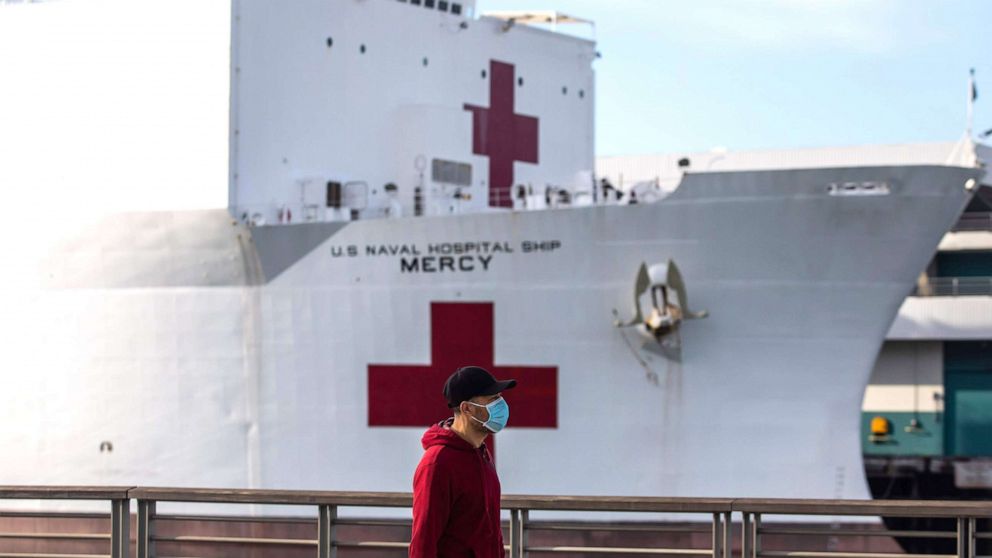 PHOTO: A man walks wearing facemak as a preventive measure against the spread of the coronavirus in front of the US Navy Hospital ship Mercy, March 28, 2020, at the Port of Los Angeles in the city of San Pedro, Calif.