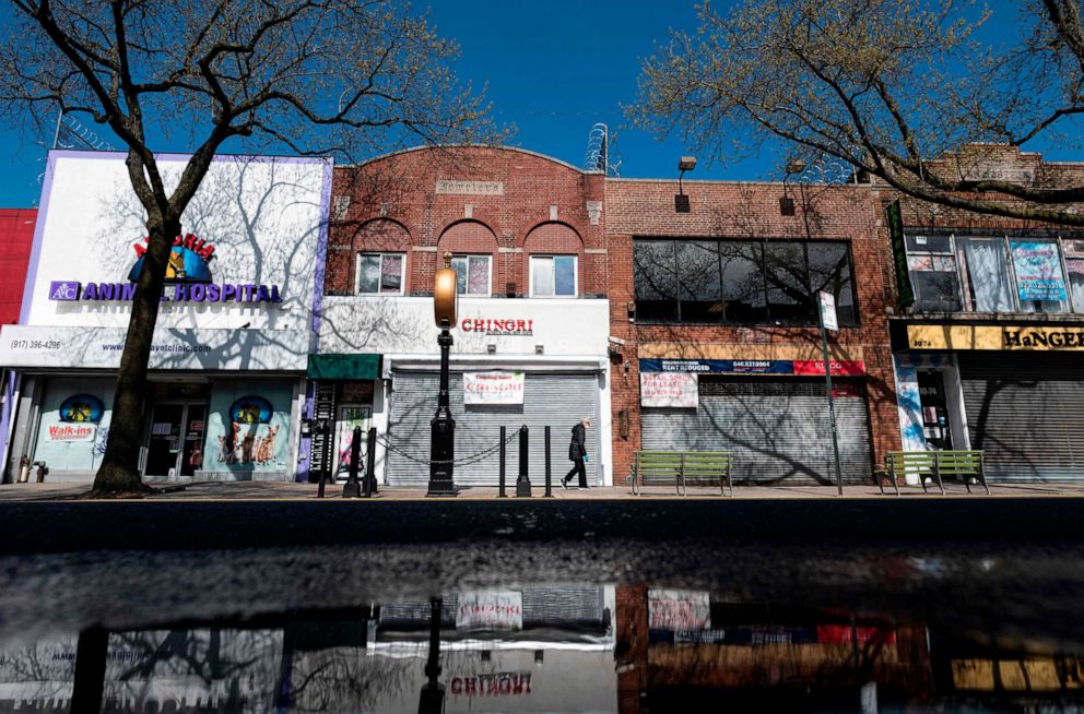 PHOTO: A woman wearing a mask walks past closed store fronts in the Astoria neighborhood of Queens, on April 15, 2020, in New York.