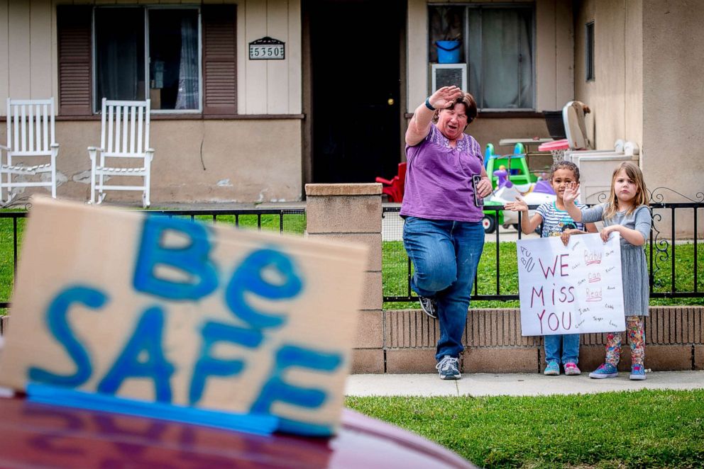 PHOTO: Students and a parent wave to their teachers and staff from Wells Middle School as they drive through the neighborhood in Riverside, Calif., March 31, 2020.