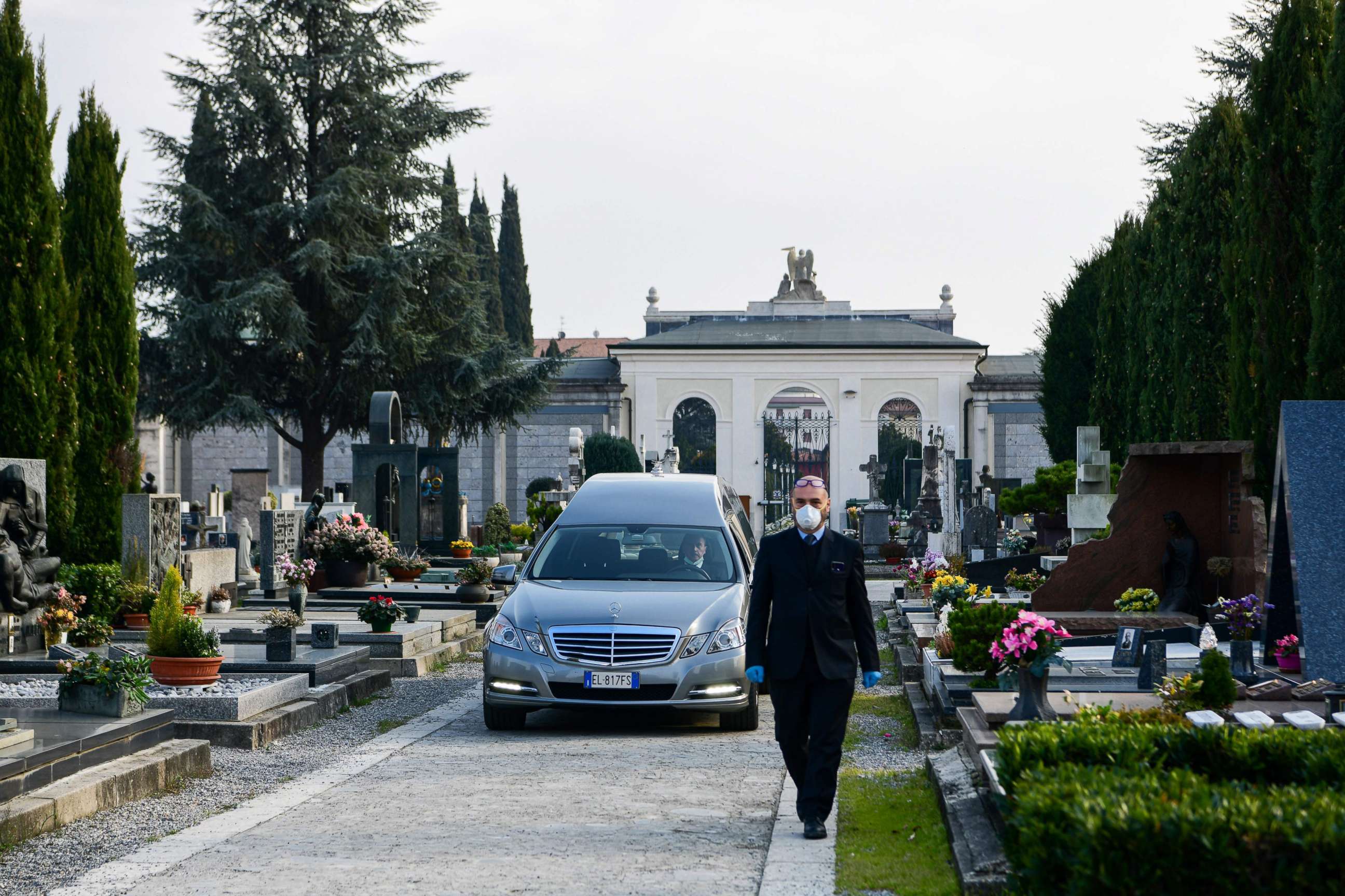 PHOTO: An undertaker wearing a face mask walks ahead of a hearse bringing the coffin of an elderly woman to a funeral service in the closed cemetery of Seriate, near Bergamo, Italy, on March 20, 2020.
