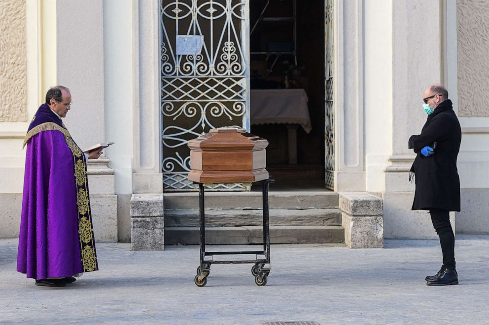 PHOTO: A man wearing a face mask stands by the coffin of his mother as a priest reads prayers during a funeral service in the closed cemetery of Seriate, near Bergamo, Italy, March 20, 2020.