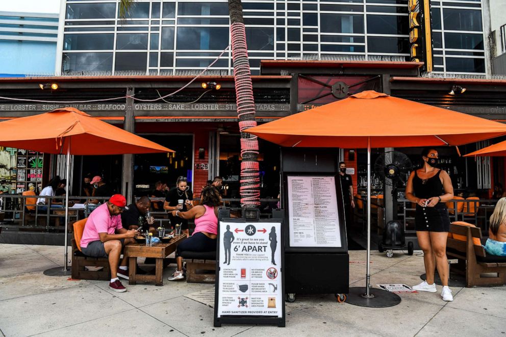 PHOTO: A sign board with precautions is kept in front of a restaurant as people eat sitting outside on Fort Lauderdale Beach Boulevard in Fort Lauderdale, Fla., May 18, 2020.