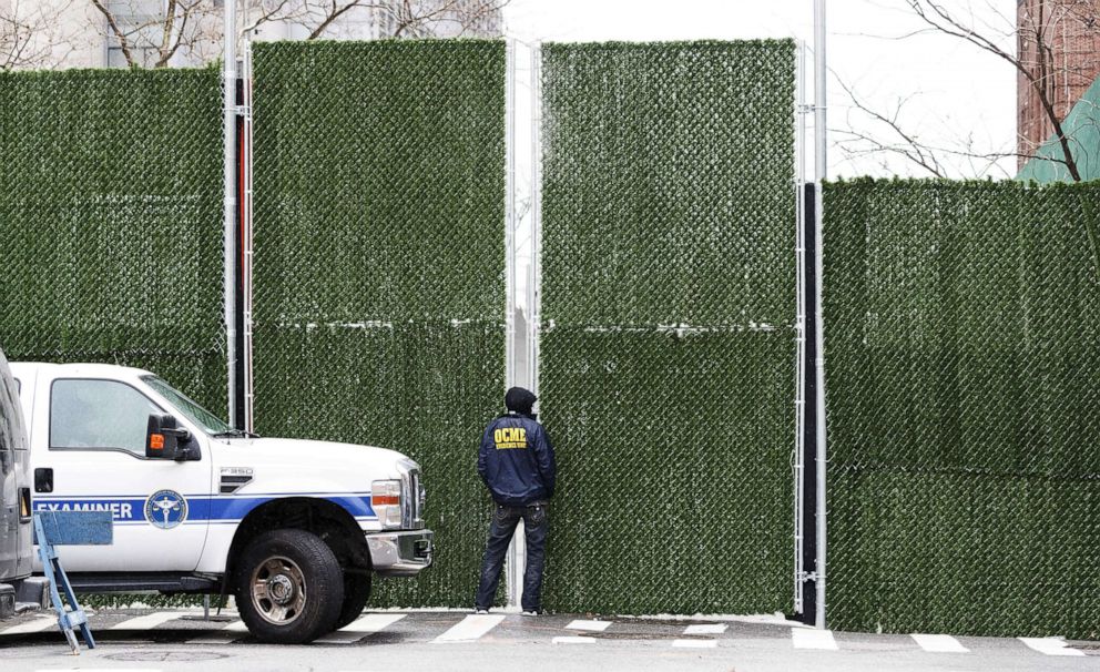 PHOTO: An employee of the office of the New York Chief Medical Examiner looks through fencing blocking a view of refrigeration trucks lined up to serve as an expanded morgue in New York, April 3, 2020.