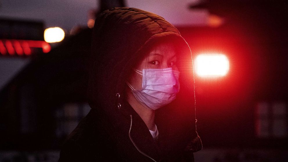 PHOTO: A Chinese woman wears a mask as she stands near the light of a police vehicle on regular duty at Beijing Railway station before the annual Spring Festival in Beijing, Jan. 21, 2020.