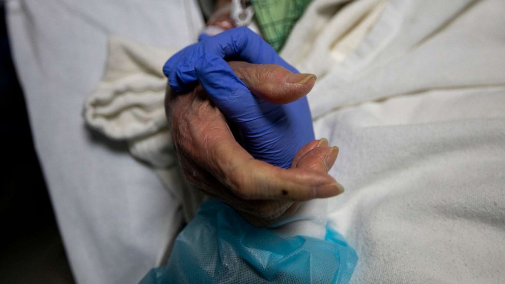 PHOTO: Registered Nurse Ana Ramos holds the hand of a 91-year-old COVID-19 patient inside the ICU at Providence St. Jude Medical Center on Dec. 25, 2020, in Fullerton, Calif.
