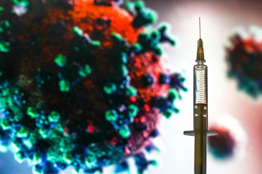PHOTO: In this photo illustration a medical syringe is seen in front of a microscopic image of coronavirus.