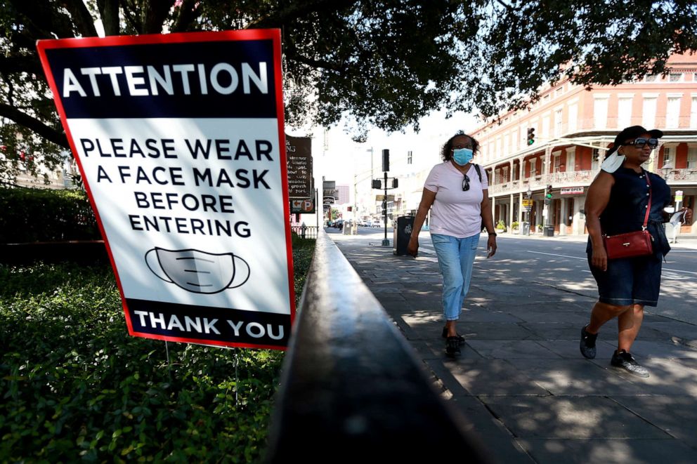 PHOTO: Visitors walk past face mask signs along Decatur Street in the French Quarter on July 14, 2020, in New Orleans.