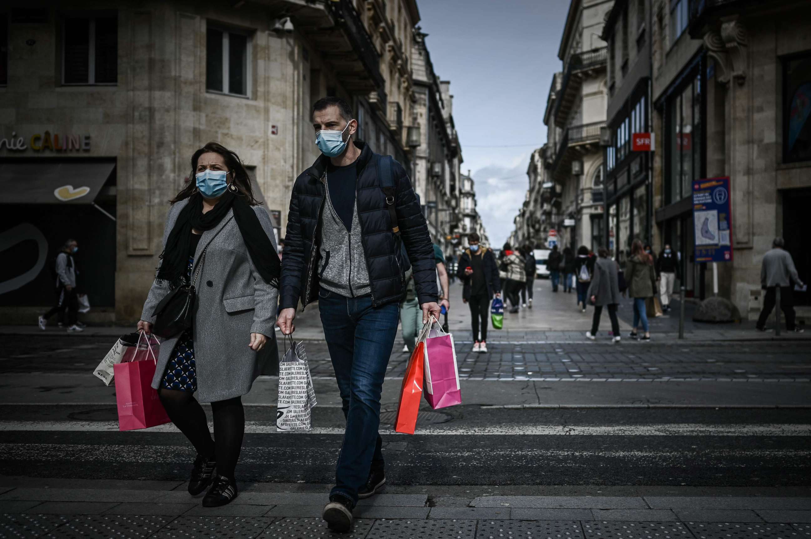 PHOTO: A man and a woman carrying shopping bags cross a street located in the mandatory face mask zone to limit Covid-19 infections in Bordeaux, Oct. 28, 2020, as France is set to put tough new measures in place.