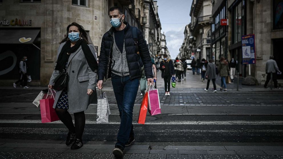 PHOTO: A man and a woman carrying shopping bags cross a street located in the mandatory face mask zone to limit Covid-19 infections in Bordeaux, Oct. 28, 2020, as France is set to put tough new measures in place.