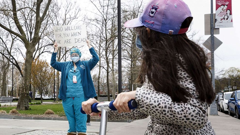 PHOTO: A child on a scooter looks at a nurse at Jacobi Medical Center participating in a rally to protest their lack of personal protective equipment, PPE, and institutional support in the Bronx borough of New York, April 17, 2020.