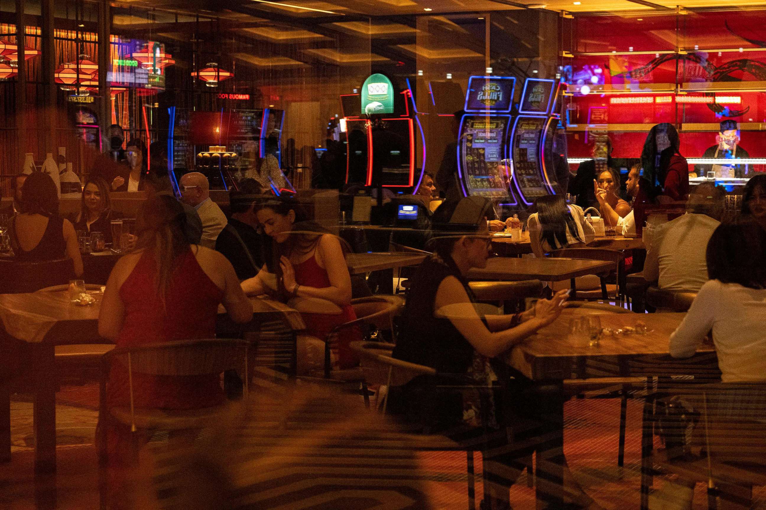 PHOTO: People gather at a restaurant, as slot machines are seen reflected in the glass, during the celebratory grand opening of Resorts World Las Vegas hotel and casino, June 24, 2021, in Las Vegas.