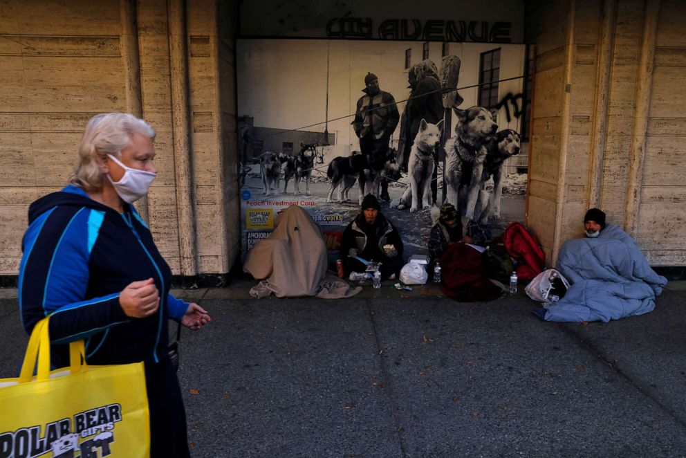 PHOTO: A woman wearing a protective face mask, amid the coronavirus disease (COVID-19) pandemic, walks by a group of men on 4th avenue in Anchorage, Alaska, U.S., October 30, 2021. REUTERS/Shannon Stapleton