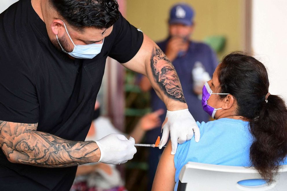 PHOTO: Respiratory therapist Robert Blas (left) from Veritas Vaccines administers the Pfizer COVID-19 vaccine to people at a mobile clinic in an East Los Angeles neighborhood, which has lower vaccination rates especially among the youth, on July 9, 2021.