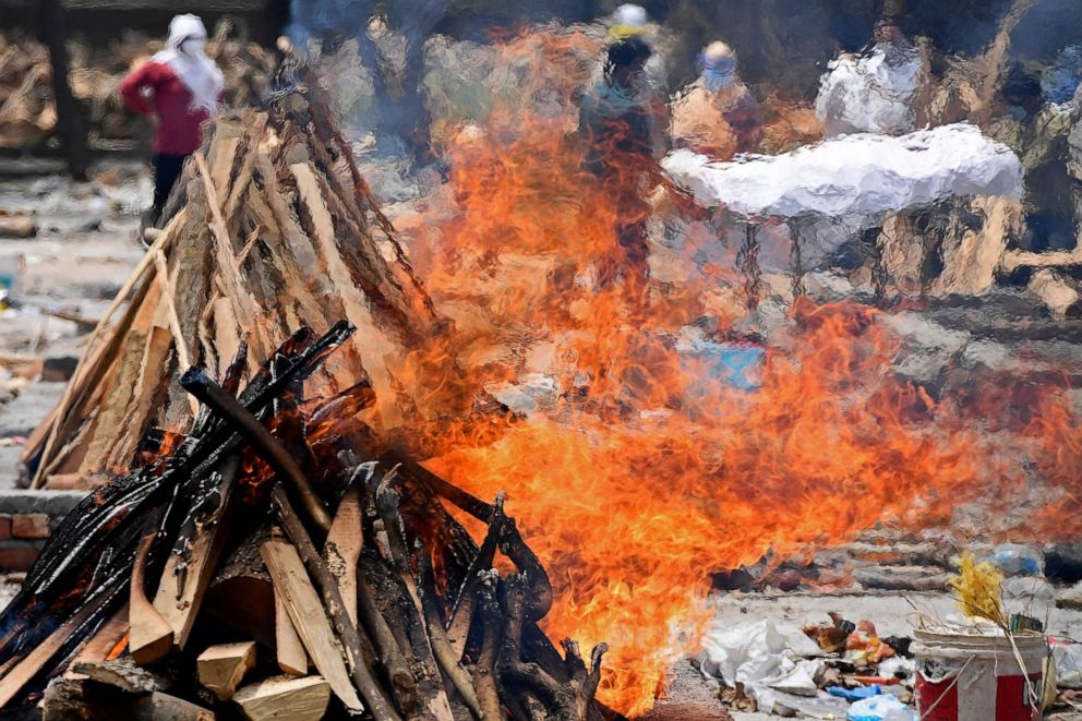 PHOTO: Family members and relatives carry the body of a victim who died of the Covid-19 coronavirus next to the burning pyres of other victims at a cremation ground in New Delhi on May 4, 2021.