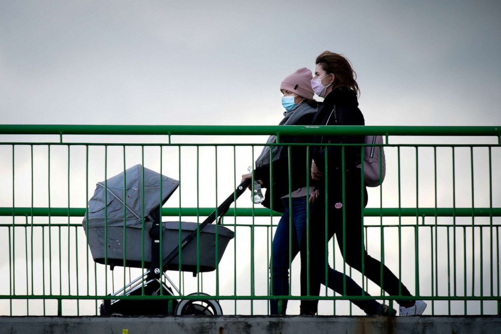 PHOTO: Two pedestrians wearing face masks cross a bridge pishing a baby carriage in Warsaw, Poland, Feb. 27, 2021.