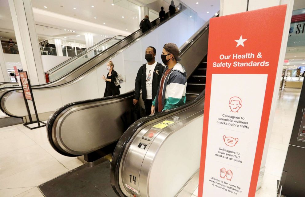 PHOTO: People wearing face masks walk past a notice board with COVID-19 preventive instructions at a Macy's store in New York, Oct. 16, 2020. 