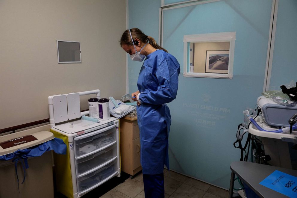 PHOTO: Registered nurse Annie Voegele puts on her personal protective equipment (PPE) gear before treating a COVID-19 patient in their isolation room at the Providence Mission Hospital in Mission Viejo, Calif., April 12, 2022.