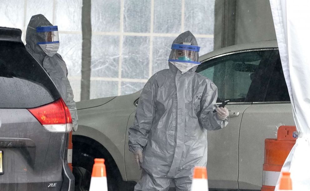 PHOTO: Workers in protective suits wait for people to be tested as they arrive by car at the State's First Drive Through COVID-19 Mobile Testing Center at Glen Island Park in New Rochelle, NY., March 13, 2020.