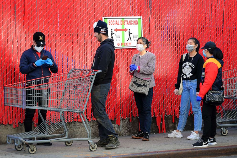 PHOTO: Customers wait in line in front of a sign recommending social distancing to enter the Industry City Costco store on April 28, 2020, in Brooklyn, New York.