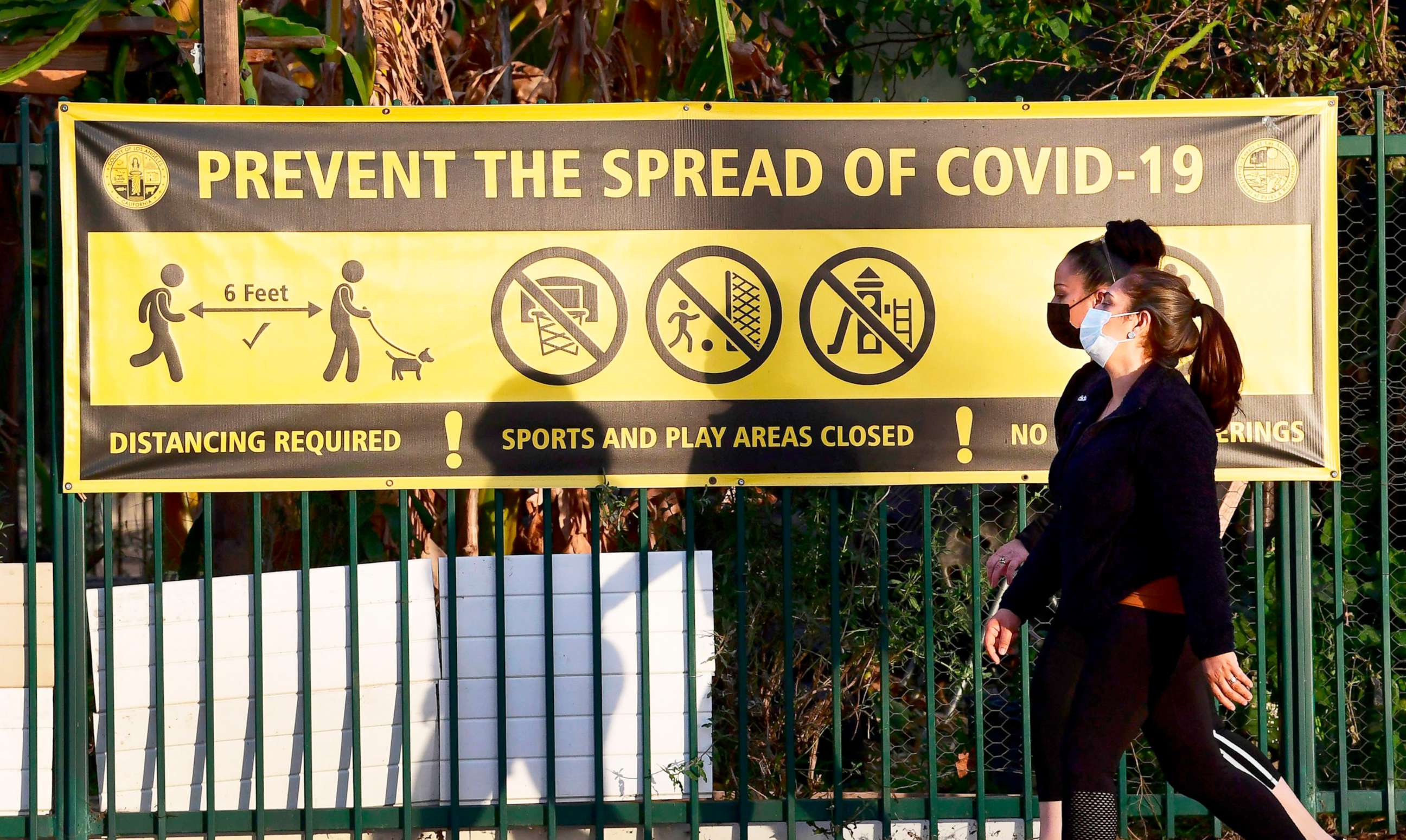 PHOTO: Pedestrians wearing facemasks walk past a prevent the spread of Covid-19 banner in Los Angeles, Jan. 19, 2020.