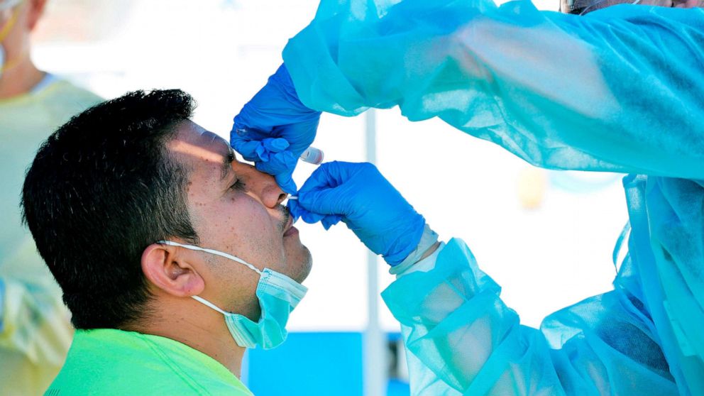 PHOTO: A health worker test a man for COVID-19 at a pop up testing location on the boardwalk at Revere Beach in Revere, Mass., on Aug. 11, 2020.