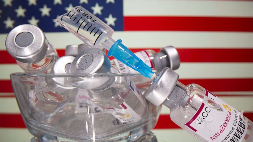 PHOTO: Vials labelled with broken sticker "AstraZeneca COVID-19 Coronavirus Vaccine" and a broken syringe are seen in front of a displayed U.S. flag in this illustration taken March 15, 2021.