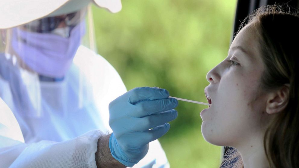 PHOTO: A healthcare worker gives a girl a throat swab test at a drive-in coronavirus testing center in Los Angeles, Aug. 11, 2020.