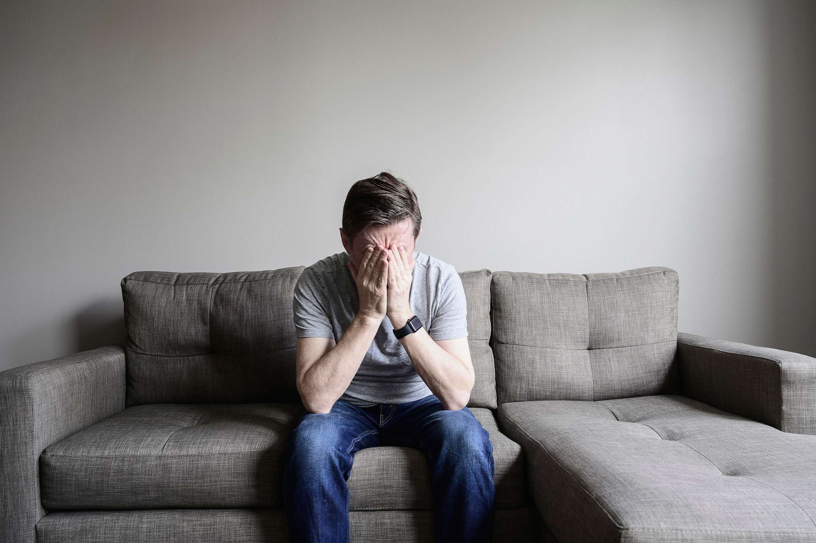 PHOTO: mature man on sofa with hands on face.