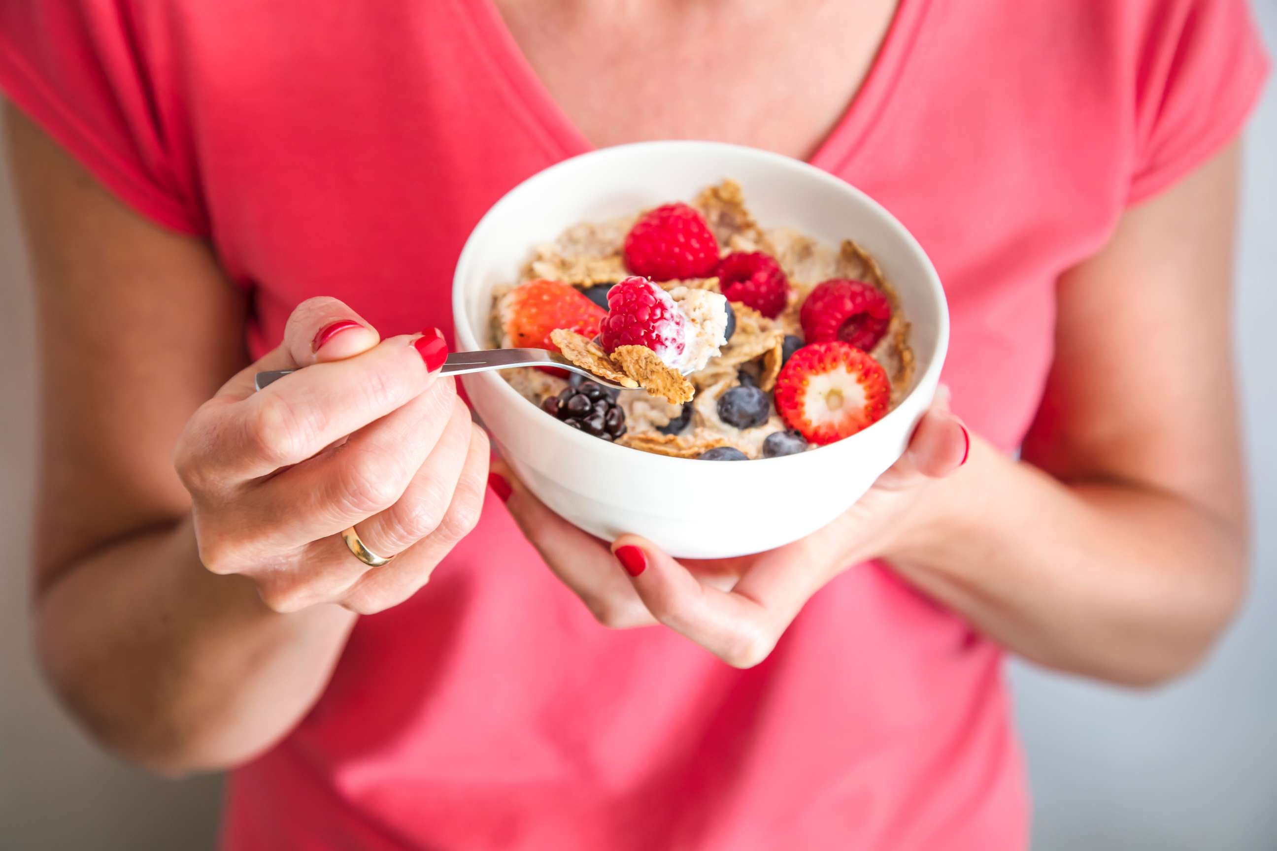 PHOTO: A woman holding a bowl containing homemade granola with oat flakes, corn flakes, dried fruits with fresh berries. 