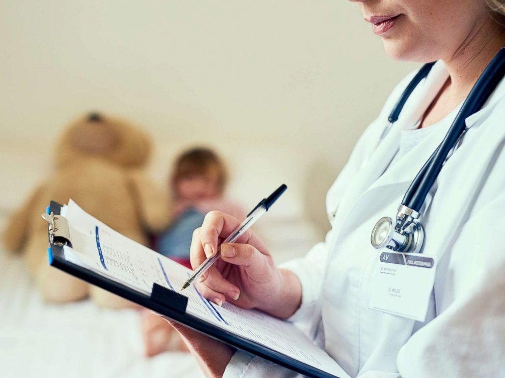 PHOTO: In the photo, a doctor fills out a form while treating a sick child.