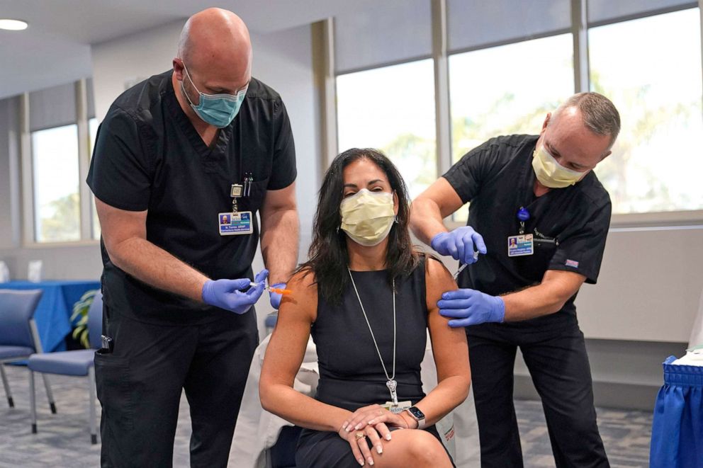 PHOTO: Dr. Lilian Abbo receives a flu vaccine from Nicholas Torres, left, and a Pfizer COVID-19 booster shot from Douglas Houghton, right, at Jackson Memorial Hospital, Oct. 5, 2021, in Miami.  