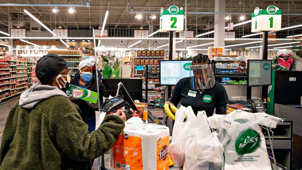 PHOTO: A cashier wearing a face shield bags groceries for a customer at the Local Market Foods store in Chicago, April, 8, 2020.