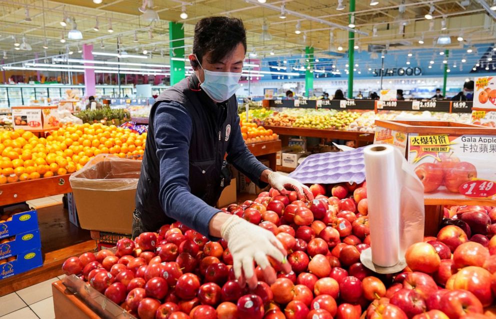 PHOTO: Wearing a mask and gloves, a worker re-stocks apples in a grocery store in Falls Church, Va., April 3, 2020. 