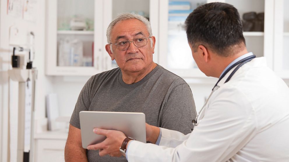 PHOTO: A doctor uses a digital tablet to talk to senior man.