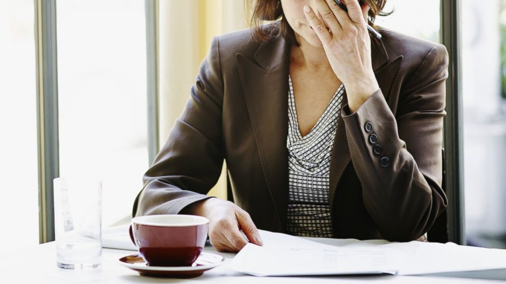 A woman sits at a table with a hand over her face in an undated stock photo.