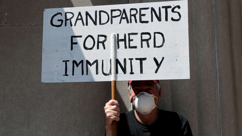 PHOTO: A demonstrator holding a sign reading "Grandparents for Herd Immunity" as protestors rally against coronavirus restrictions during a rally held outside the Pennsylvania state Capitol Building in Harrisburg, Pa., May 15, 2020. 