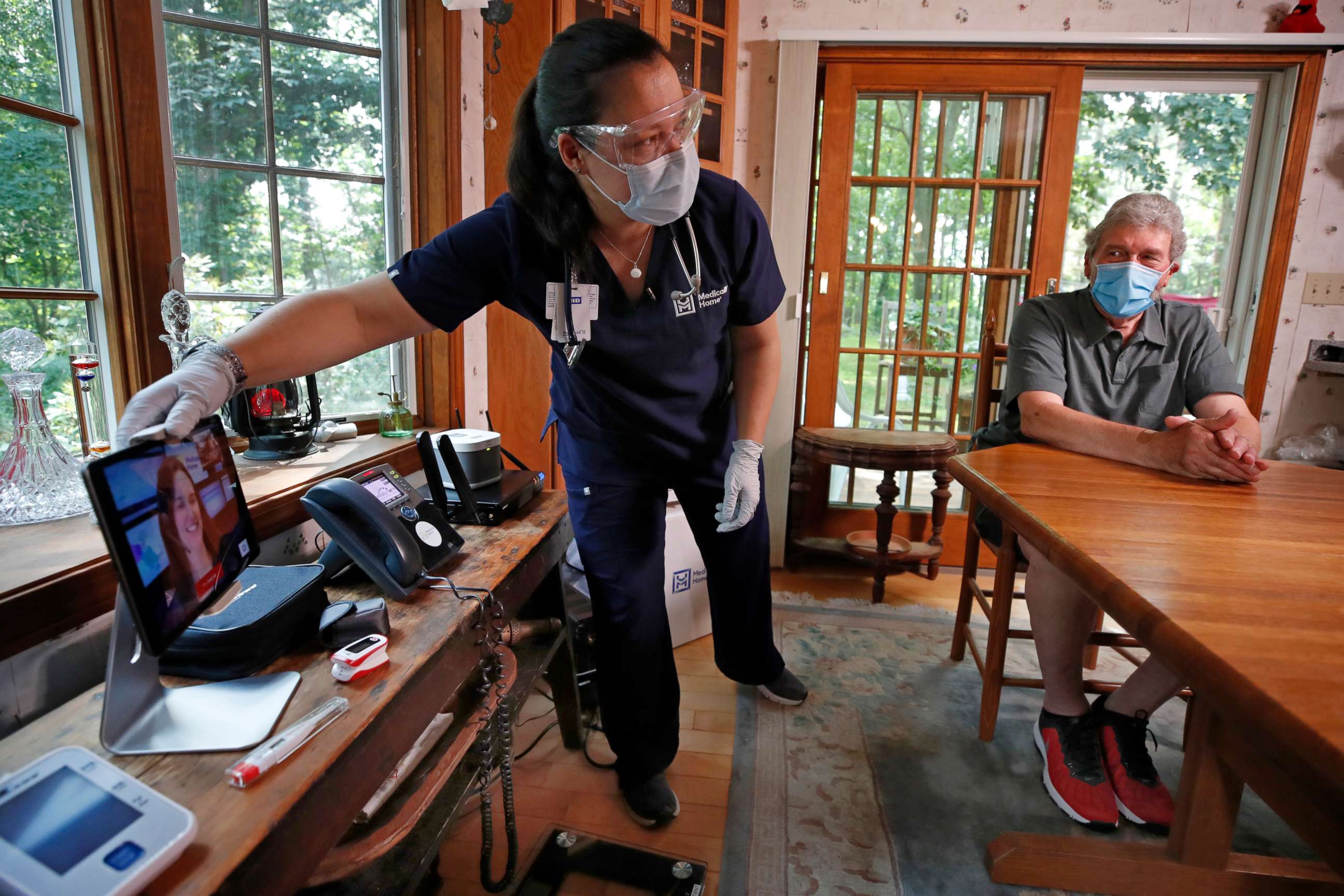 PHOTO: Nurse practitioner Sadie Paez picks up a tablet to set up a telehealth session for William Merry, who is recovering from pneumonia at his home, Thursday, July 9, 2020, in Ipswich, Mass. 