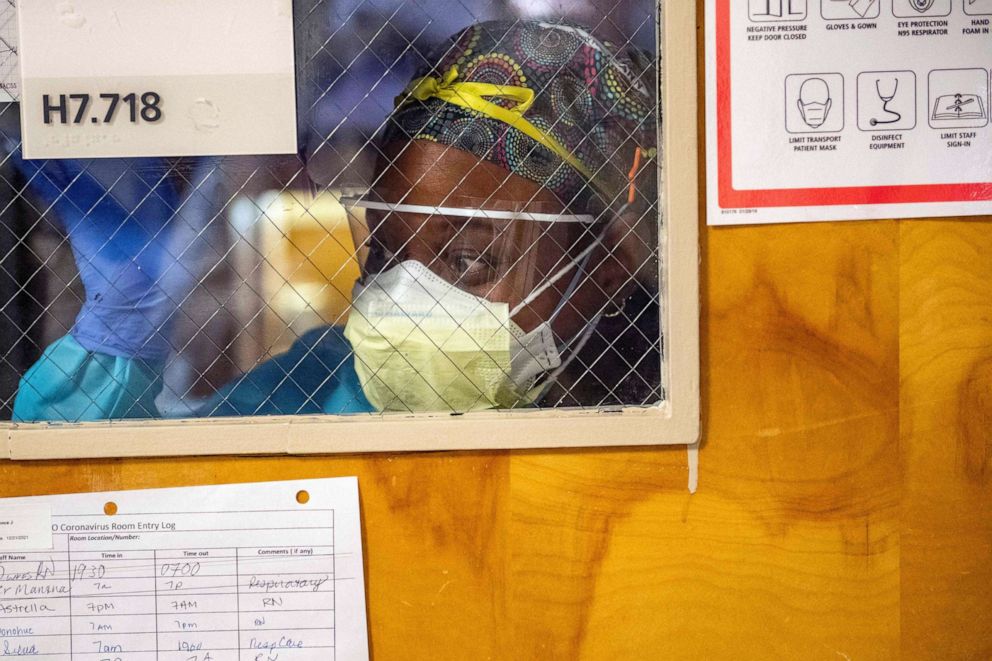 PHOTO: A medical worker waves to a colleague, through the window of a negative pressure room with a Covid-19 patient, asking for medical supplies in the ICU ward at UMass Memorial Medical Center in Worcester, Mass., Jan. 4, 2022.