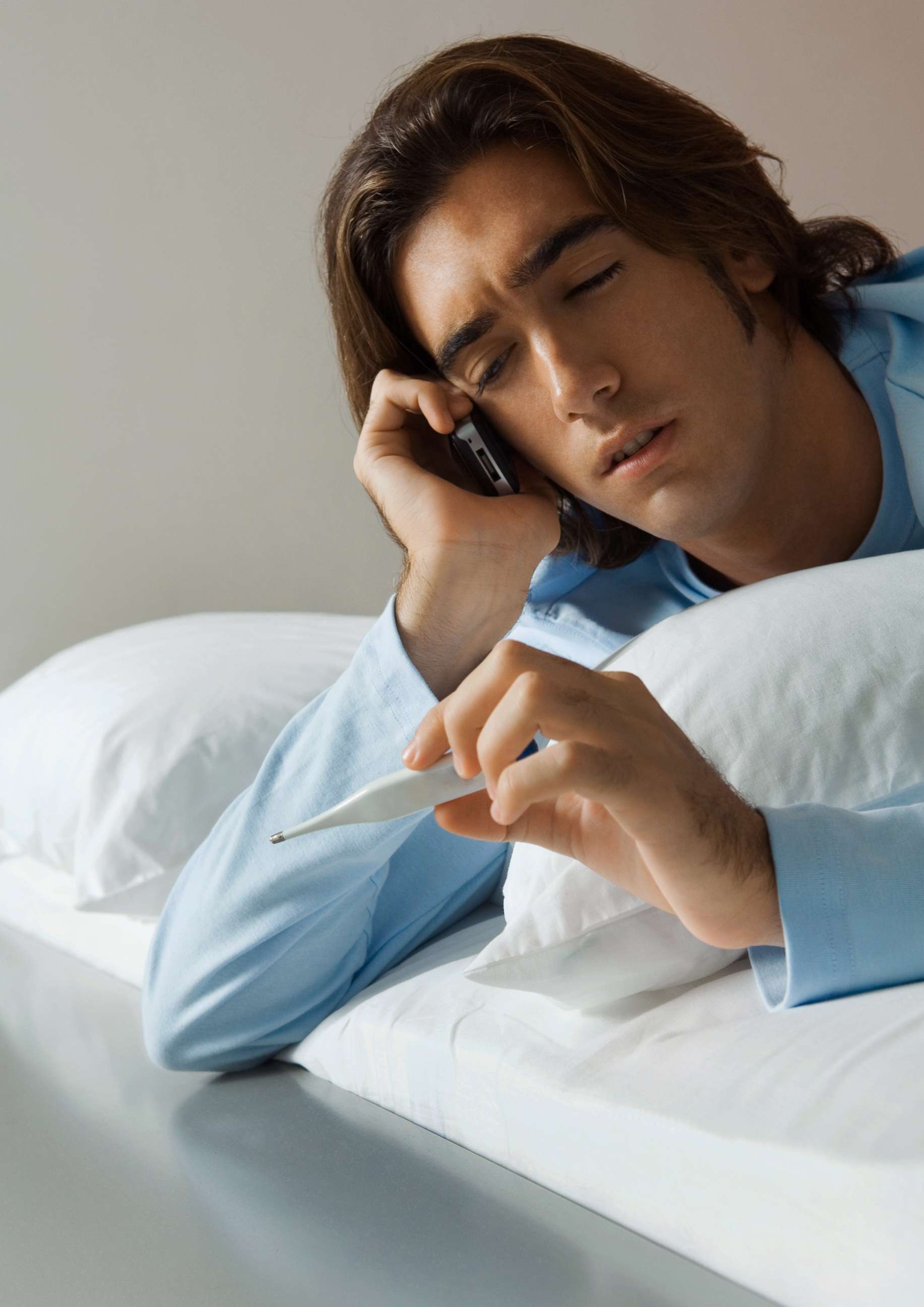 PHOTO: A man is pictured lying in bed, using a cell phone and holding up thermometer in this undated stock photo.