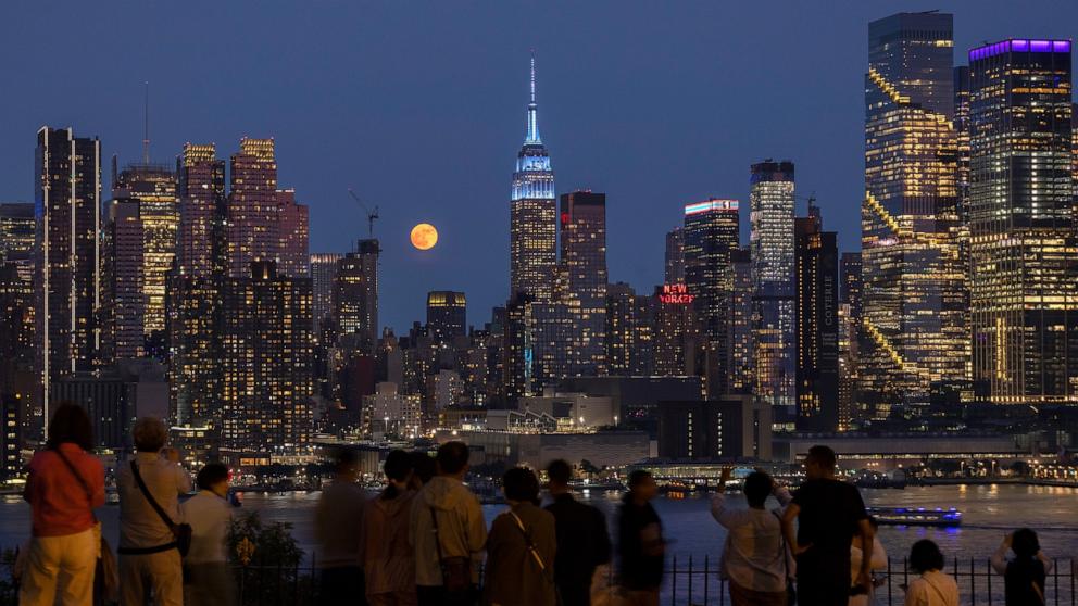 PHOTO: People watch the full Strawberry Moon rise behind the skyline of midtown Manhattan and the Empire State Building in New York City, June 10, 2025.