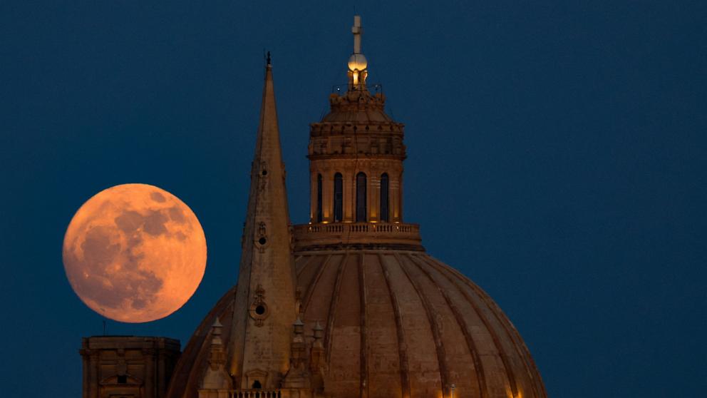 PHOTO: A full moon known as the Strawberry Moon rises behind the steeple of St Paul's Anglican Cathedral and the dome of the Basilica of Our Lady of Mount Carmel in Valletta, as seen from Sliema, Malta, June 10, 2025. 