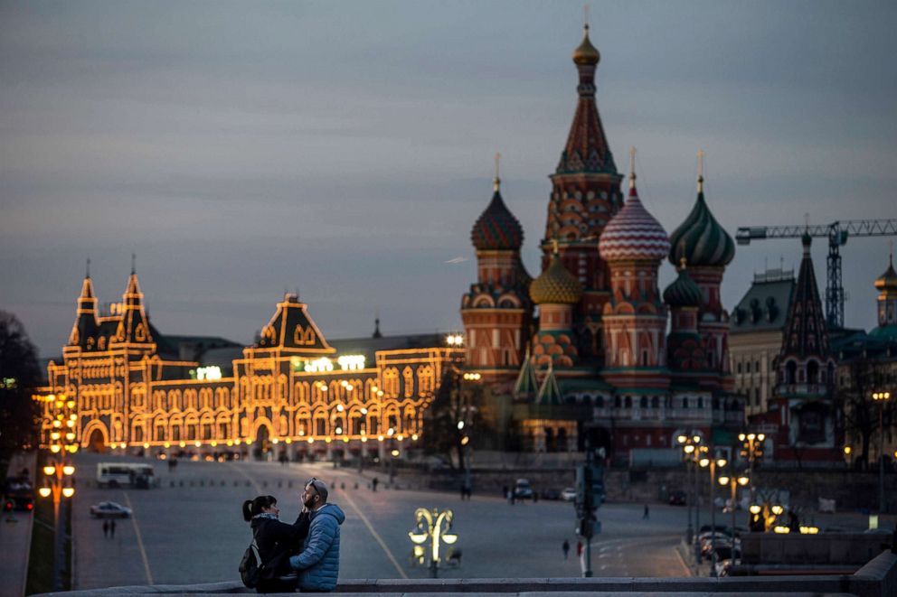 PHOTO: A couple enjoy warm weather on a bridge with St. Basil's Cathedral, right, and an almost empty Red Square after sunset in Moscow, March, 28, 2020.