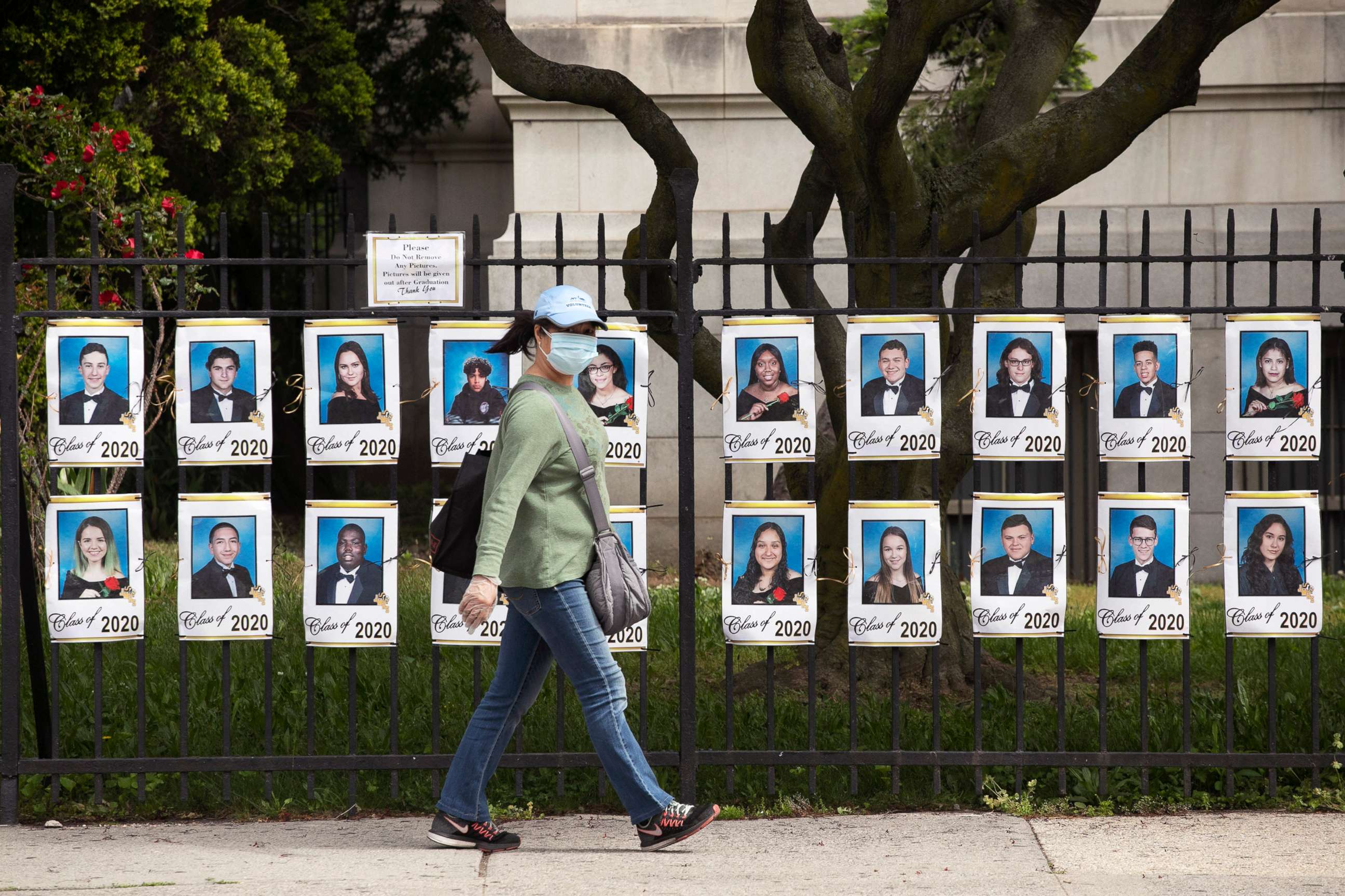 PHOTO: A woman passes by photographs of the graduating class of 2020 in front of James Madison High School, May 27, 2020, in the Brooklyn borough of New York.