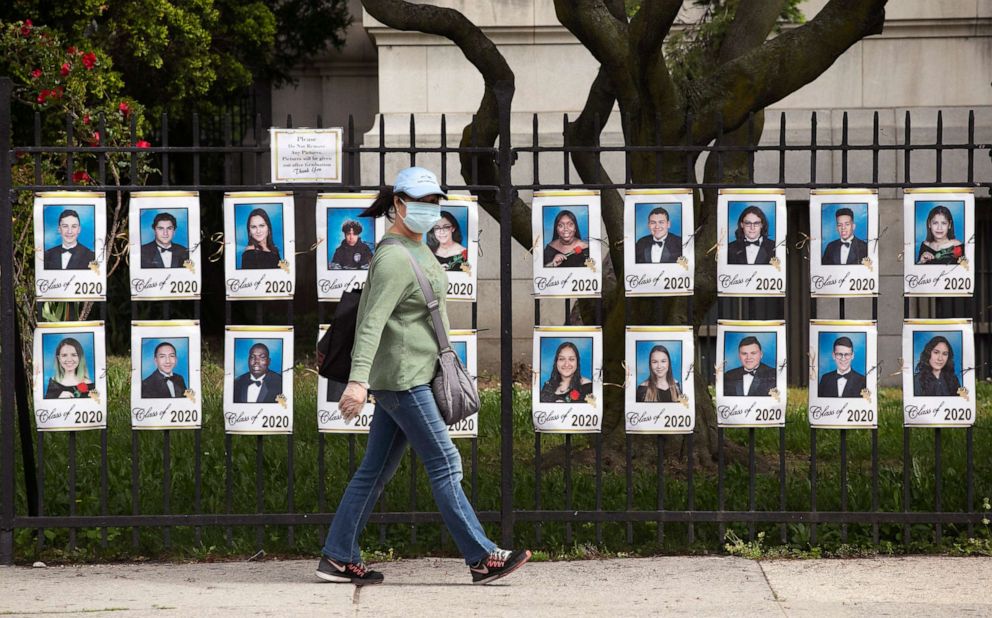 PHOTO: A woman passes by photographs of the graduating class of 2020 in front of James Madison High School, May 27, 2020, in the Brooklyn borough of New York.