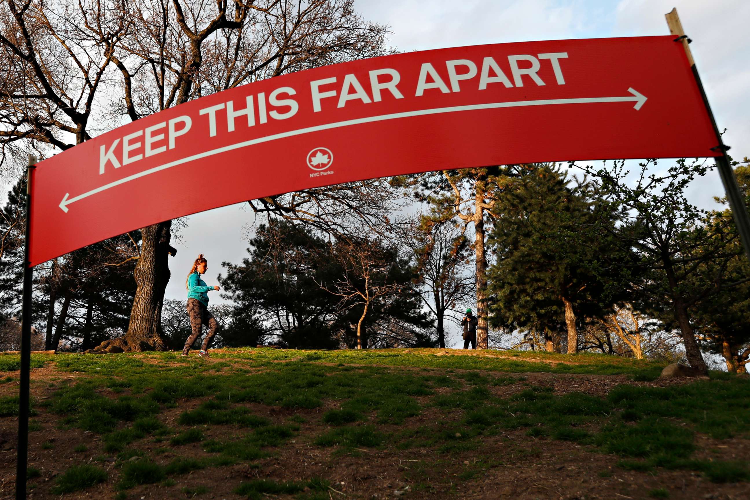 PHOTO: A woman jogs in Brooklyn's Fort Greeene park, April 5, 2020, beneath a sign demonstrating the distance people should keep from each other during the coronavirus outbreak in New York.