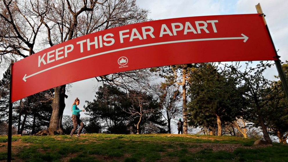 PHOTO: A woman jogs in Brooklyn's Fort Greeene park, April 5, 2020, beneath a sign demonstrating the distance people should keep from each other during the coronavirus outbreak in New York.