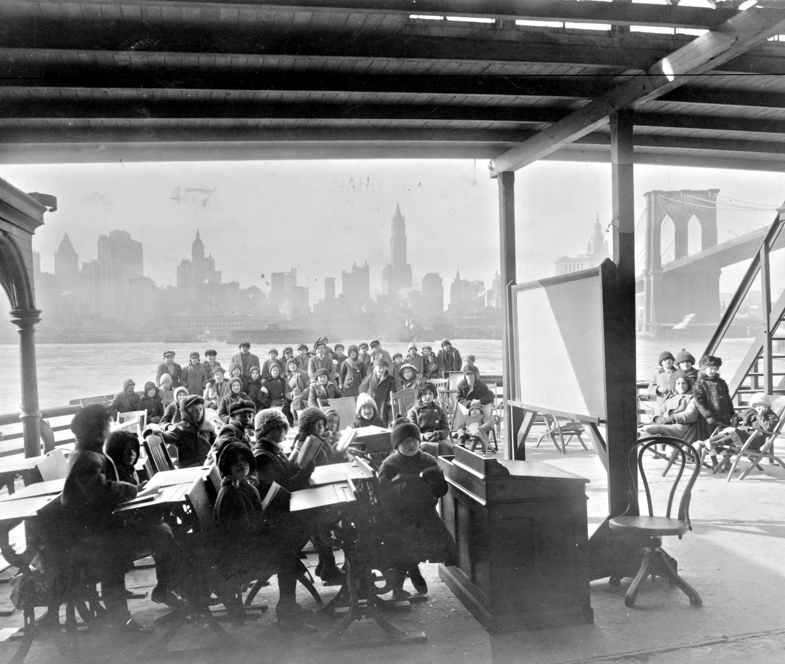 PHOTO: An open air class on a ferryboat with Manhattan and the Brooklyn Bridge in the background, 1911.