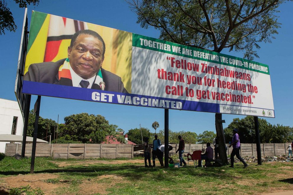 PHOTO: People seek shade under a billboard of Zimbabwe's President encouraging citizens to get vaccinated, Nov. 30, 2021, in Harare, Zimbabwe. 